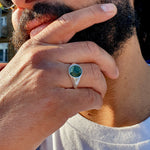 photo of a hand wearing the signet round in solid sterling silver with a emerald in the ring finger